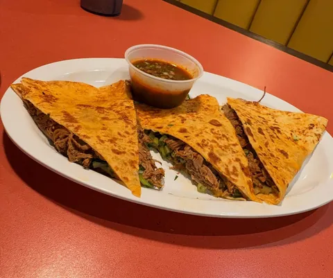 Quesabirria cut into wedges, with a cup of consommé for dipping