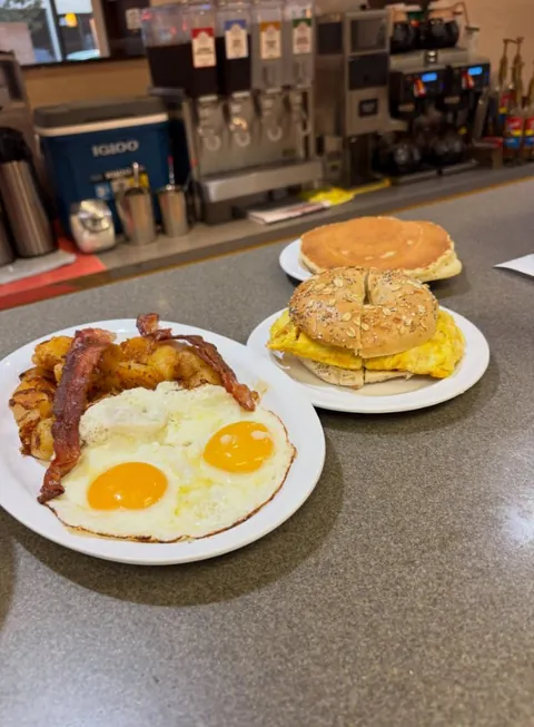 Sunny-side-up eggs with bacon and home potatoes, an egg and cheese bagel and a pancake on the Sunrise counter