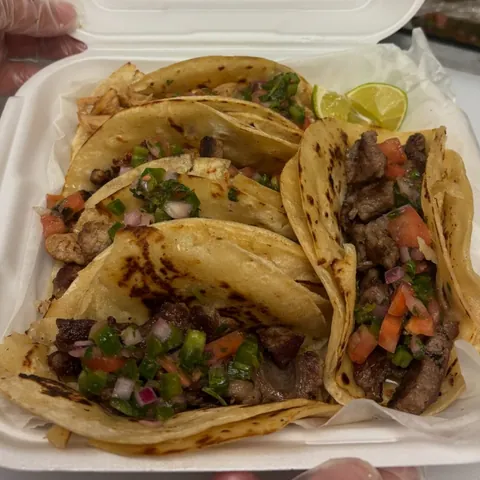 A to-go box of street tacos with pico de gallo and lime